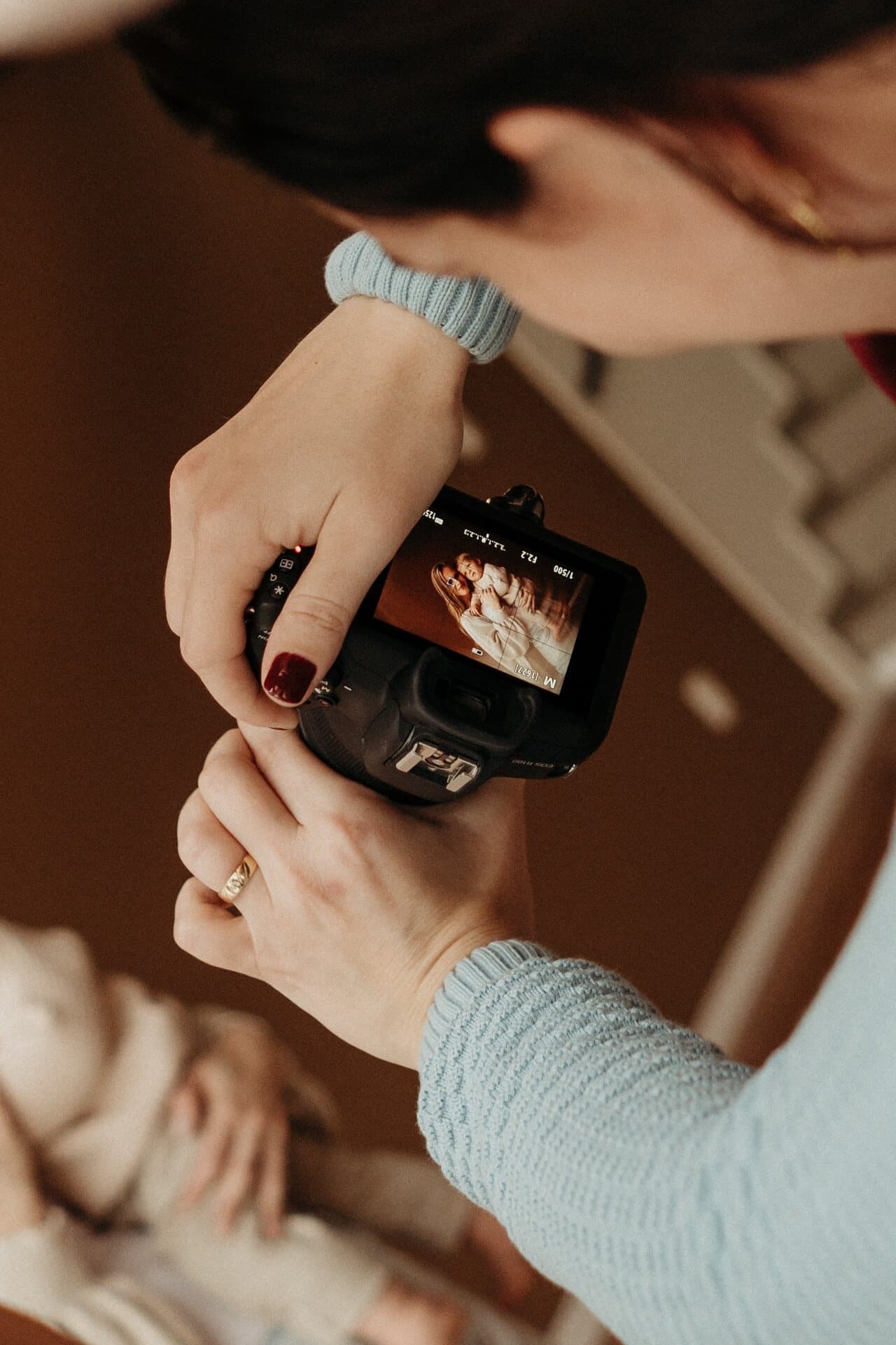 Mãos da fotógrafa segurando a câmera, com a foto do recém-nascido recém-clicada aparecendo na tela
